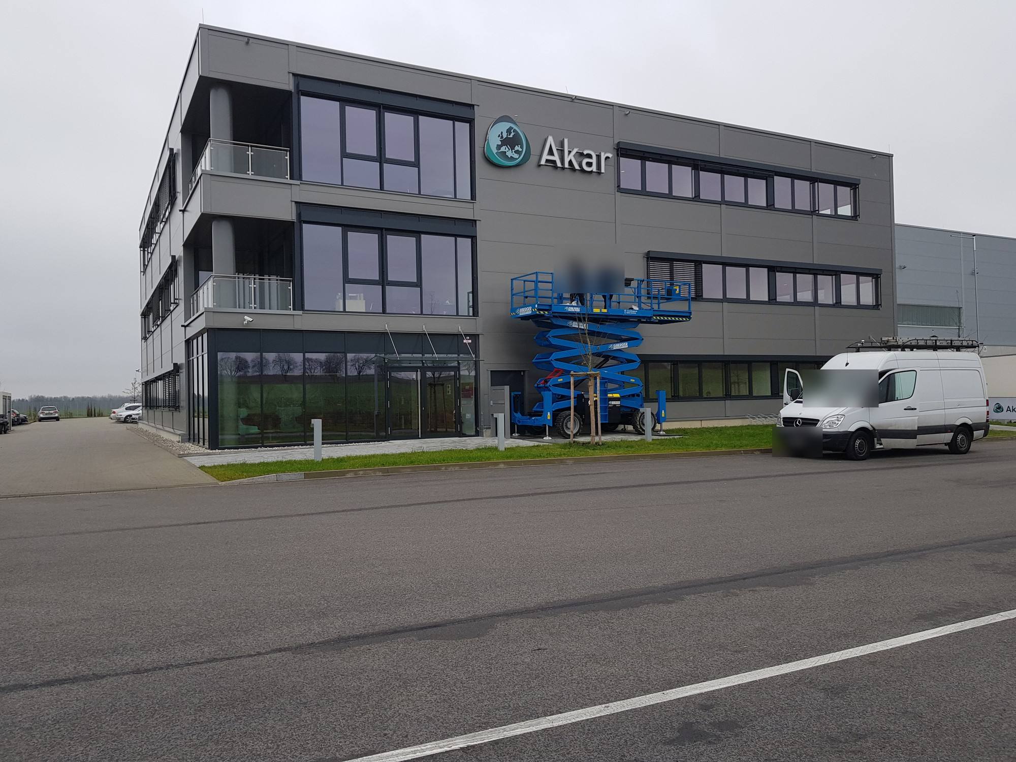 Bürogebäude von Akar bei Tag, Monteure auf einer Arbeitsbühne an der Fassade, daneben ein Transporter