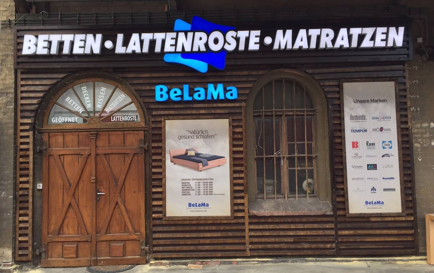 Ladenfassade aus dunklem Holz mit Schriftzug „Betten · Lattenroste · Matratzen“ und Logo „BeLaMa“ bei Tag