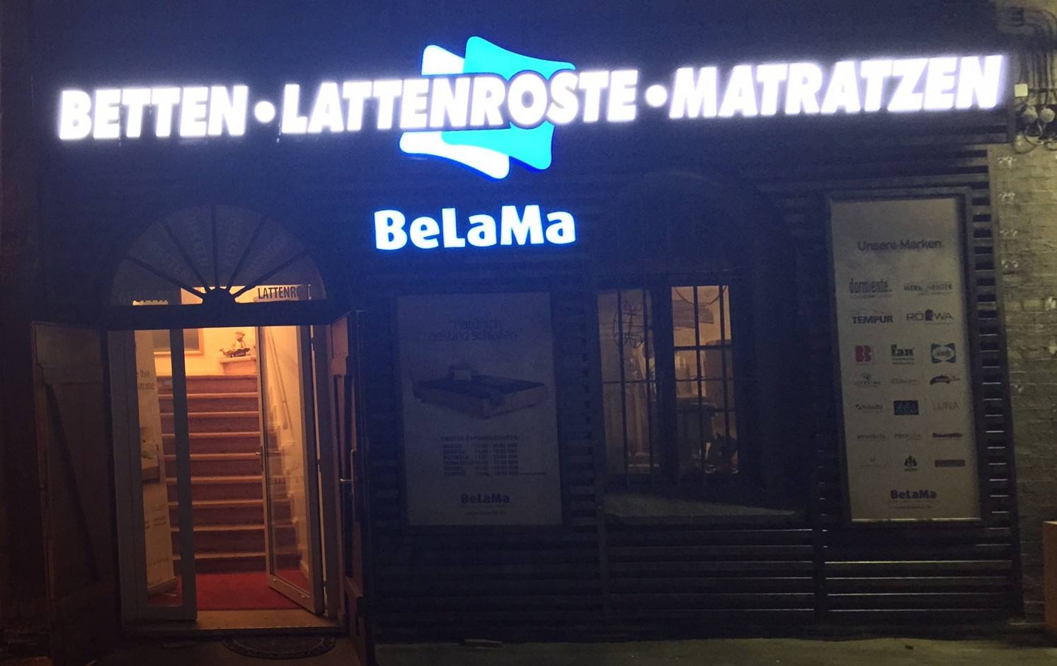 Dieselbe Fassade bei Nacht: Schriftzug leuchtet weiß, Logo blau
