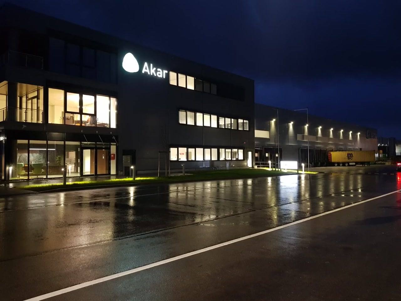 Akar office building at night with illuminated logo, wet road