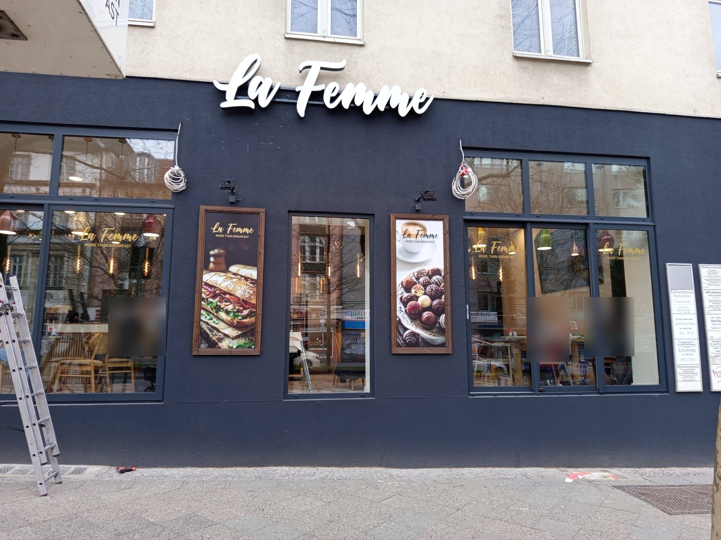 Café La Femme: Schriftzug auf dunkler Fassade, Schaufensterbilder