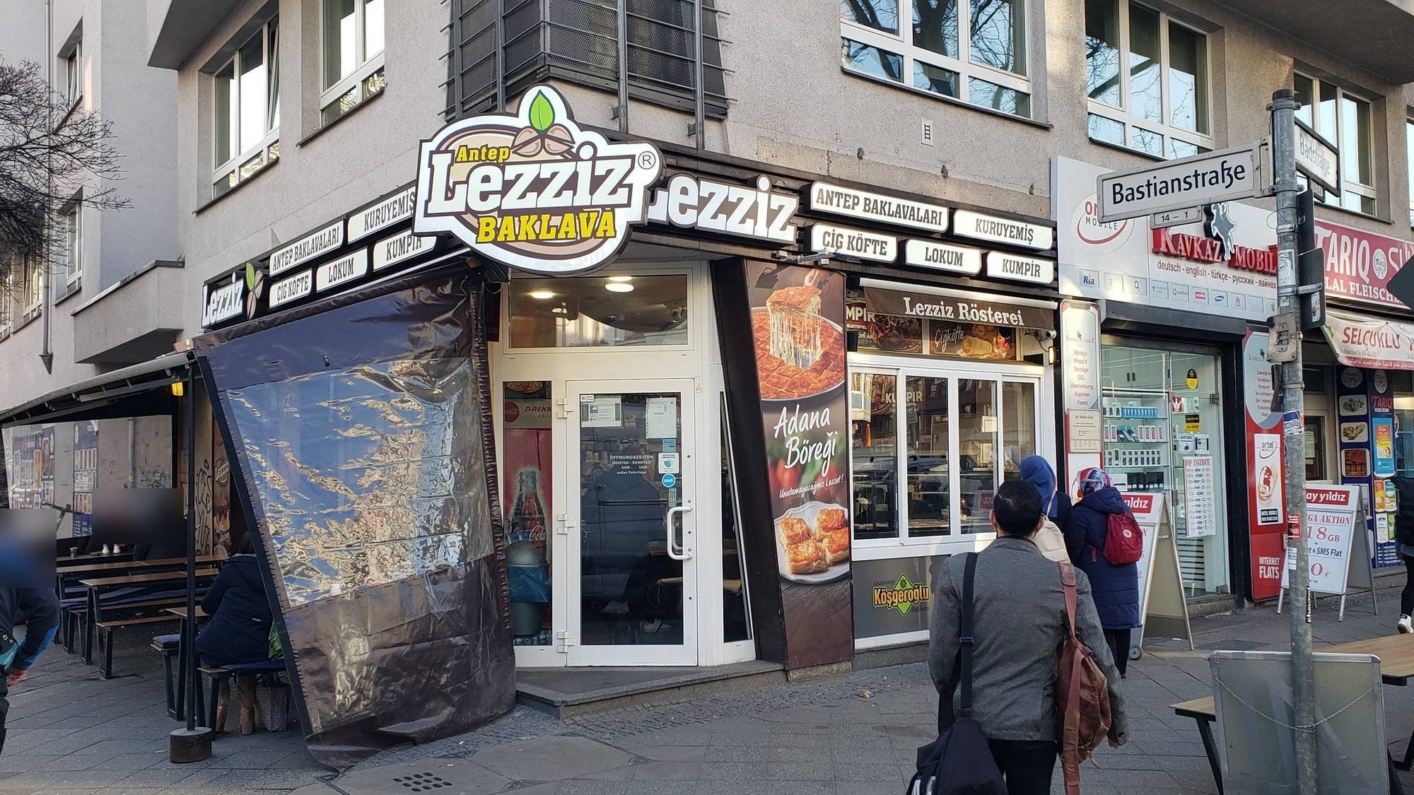 Ausgeführte Eckfassade von Lezziz in Berlin bei Tag: rundes Logo „Antep Lezziz Baklava“, Schriftzug und Leuchtkästen