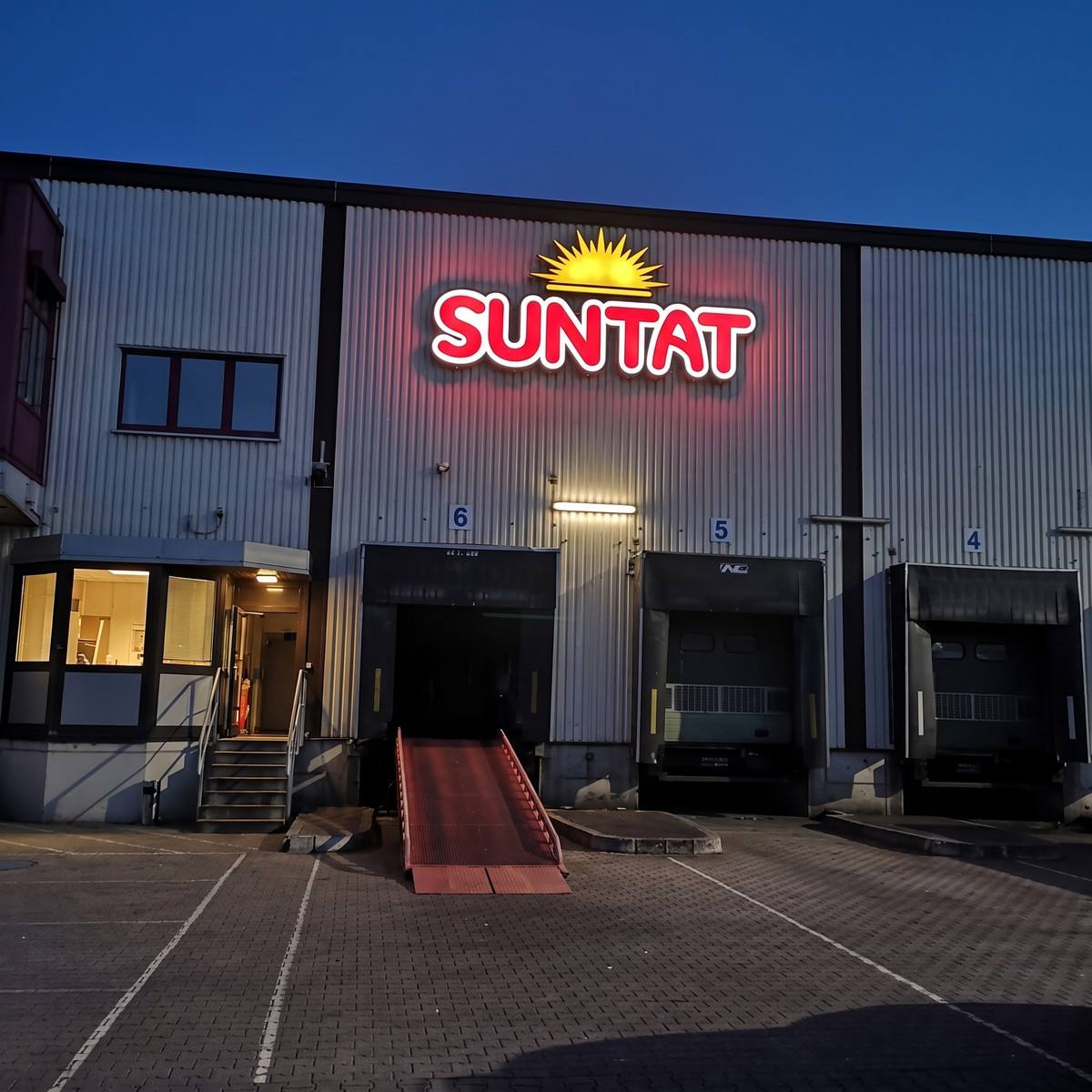 Dieselbe Halle als Nachtansicht visualisiert: rote Buchstaben und Sonnenlogo leuchten