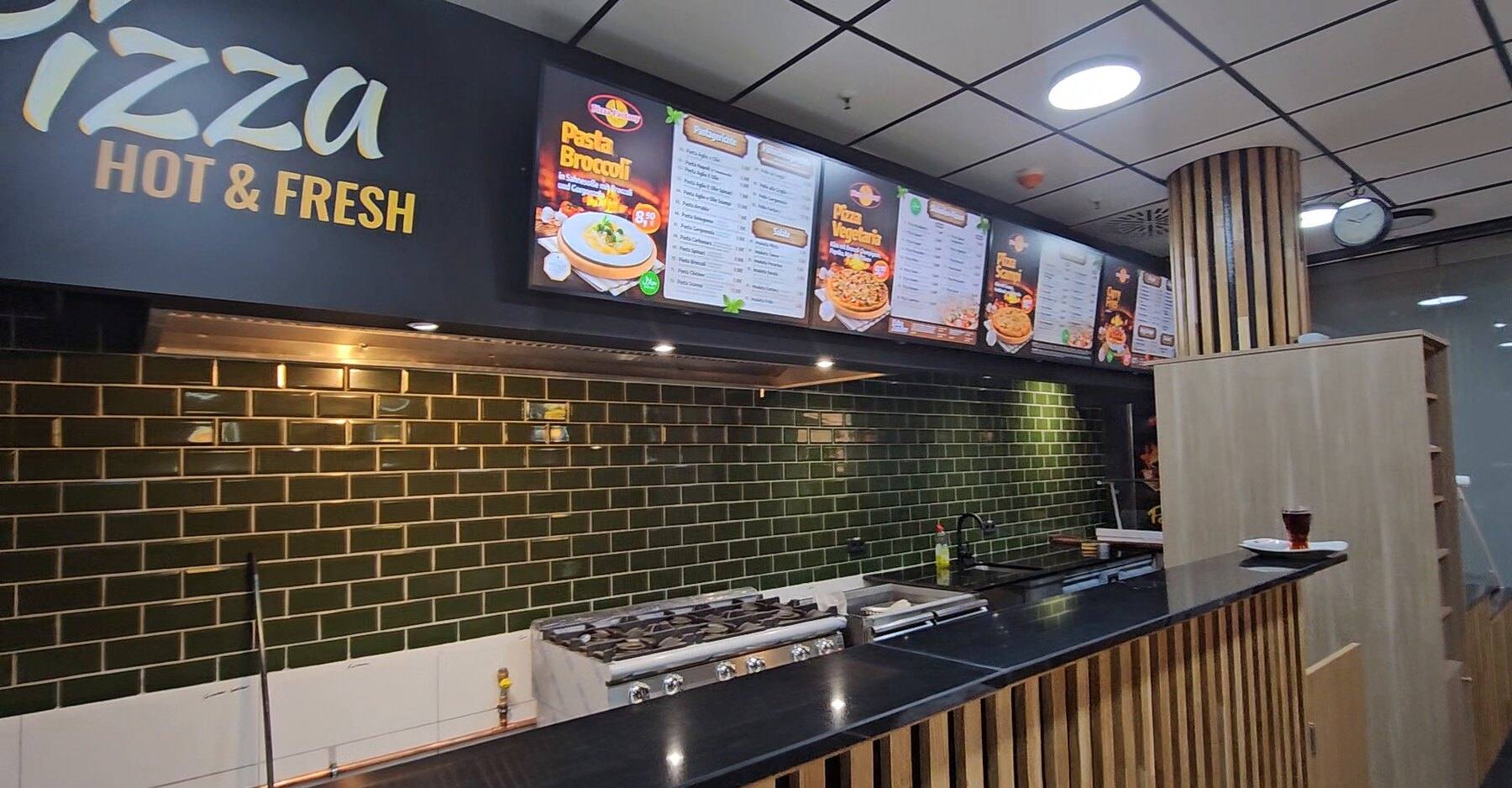 Counter at Pizza Factory with three menu screens above the kitchen and a “Pizza hot & fresh” wall graphic, content from WSCREEN