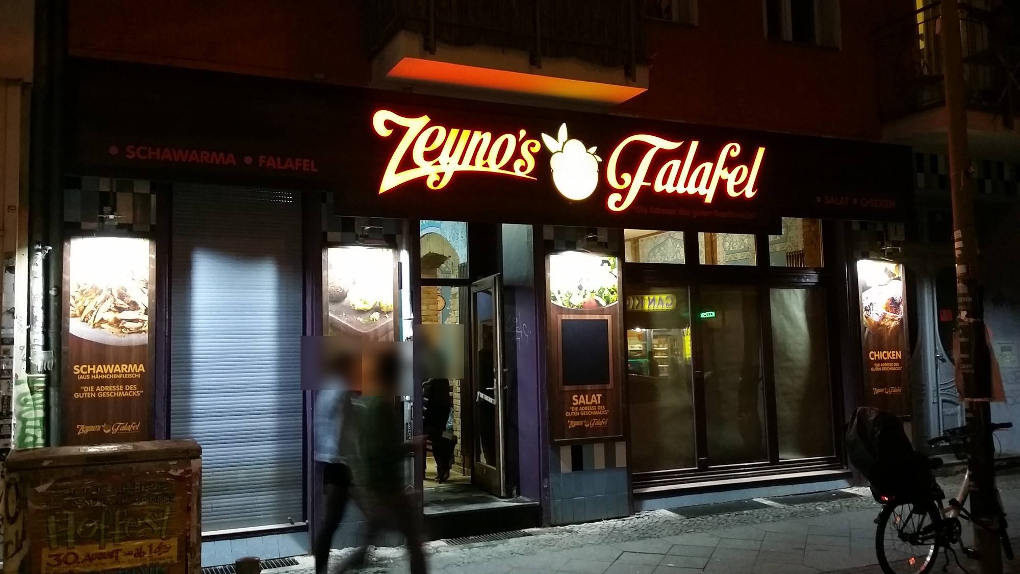 Dieselbe Fassade bei Nacht: Schriftzug leuchtet warm, Leuchtkästen beleuchten die Plakate